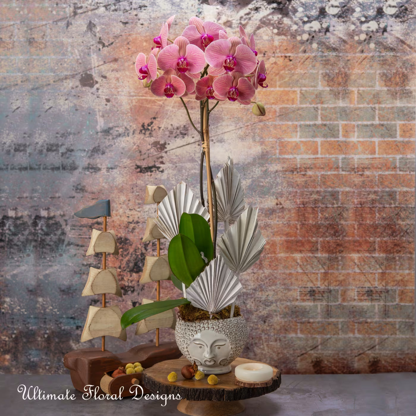 Decorative arrangement with pink orchids, a stone face vase, and fans created by ultimate floral designs in great falls va