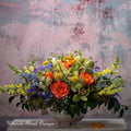 Colorful floral arrangement in a white vase with a textured pink background, featuring 'Ultimate Floral Designs' branding.