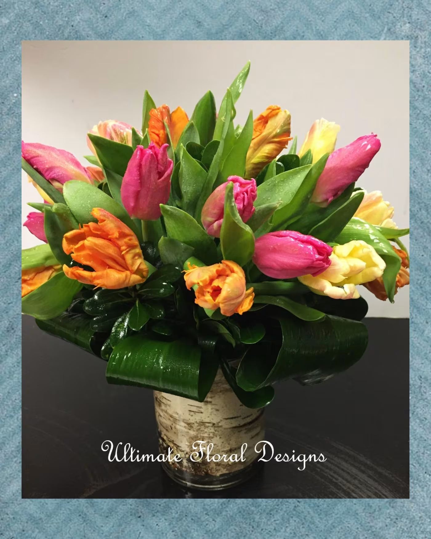 Bouquet of colorful tulips in a glass vase with 'Ultimate Floral Designs' branding.