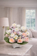White ranunculus, peach roses, and phalaenopsis orchids in a low white ceramic footed bowl — romantic arrangement by Ultimate Floral Designs
